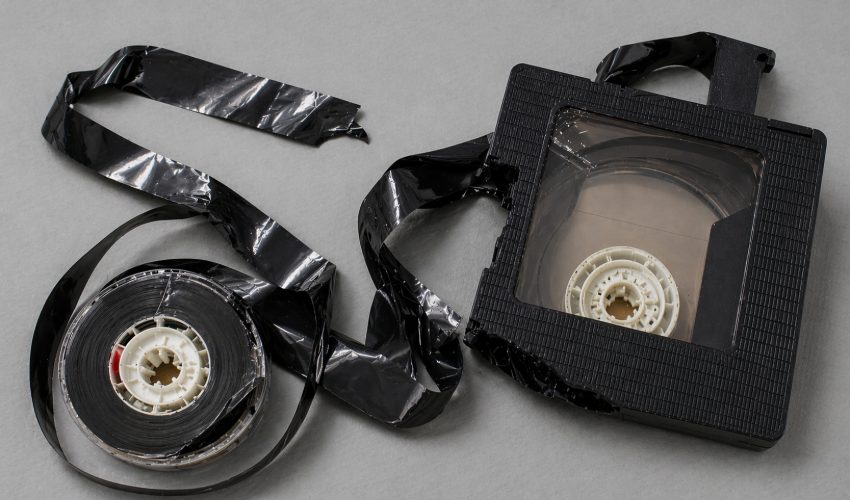 A cracked VHS cassette showing an internal reel hub and loose magnetic tape ribbon spilling out of the broken housing, illustrating what a creased and broken tape looks like after transport mechanism failure